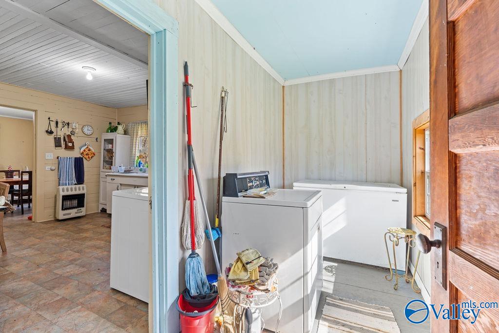 Laundry room with a washer, chest freezer, and cleaning tools beside an open doorway.