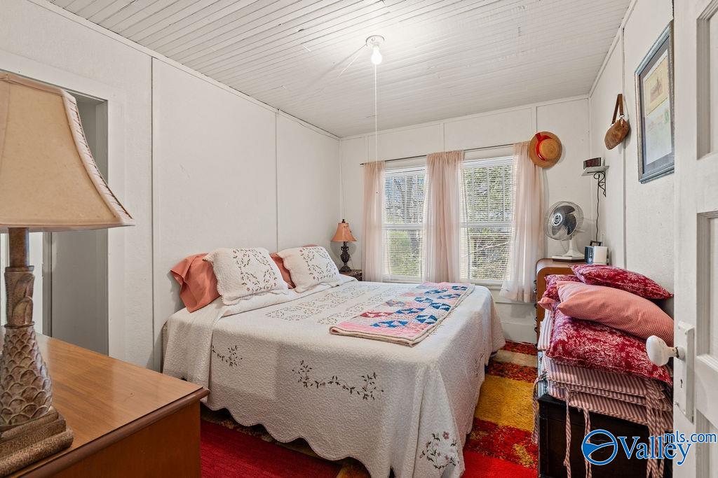 Furnished bedroom with two beds, floral bedding, a colorful quilt, and bright patterned rugs.