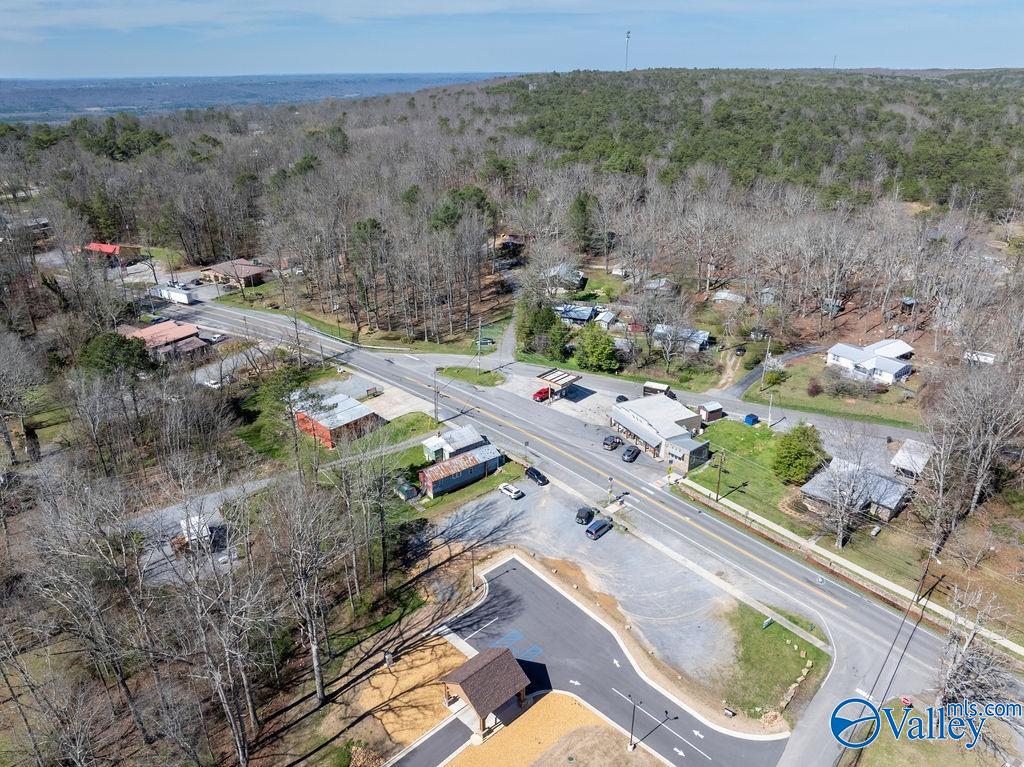 Aerial view of a highway intersection, roadside businesses, parking lot, and wooded hills.