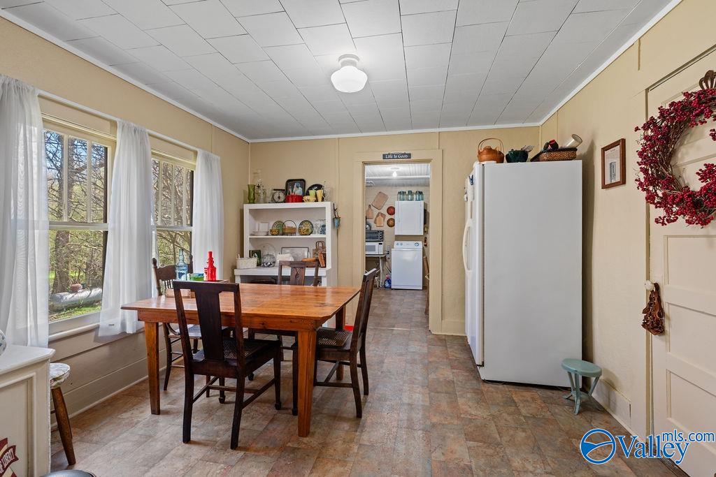 Dining room with a wooden table, curtained windows, and a view into the kitchen.