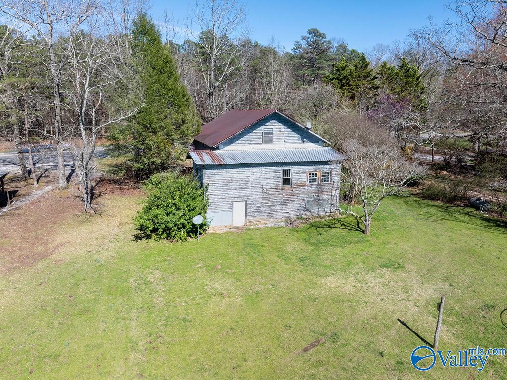 Aerial view of a weathered house with a metal awning roof and a broad grassy yard.
