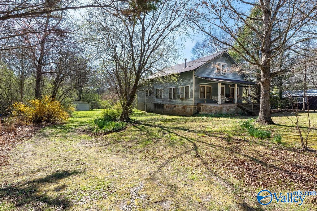 Blue-gray house with a covered porch and stone foundation, surrounded by mature trees and a grassy yard.