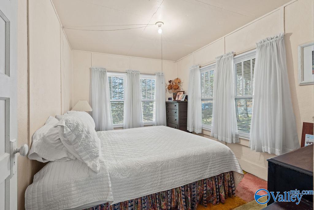 Furnished bedroom with a white quilted bed, several curtained windows, and a dark chest of drawers.