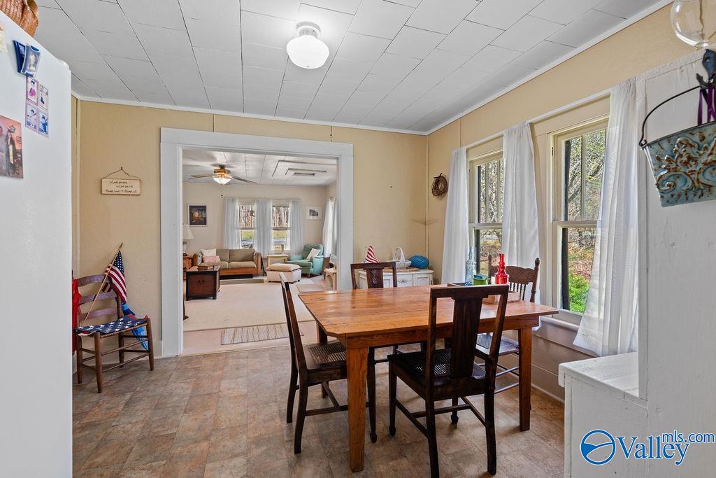 Dining room with a wooden table, tall curtained windows, and an adjoining living room.