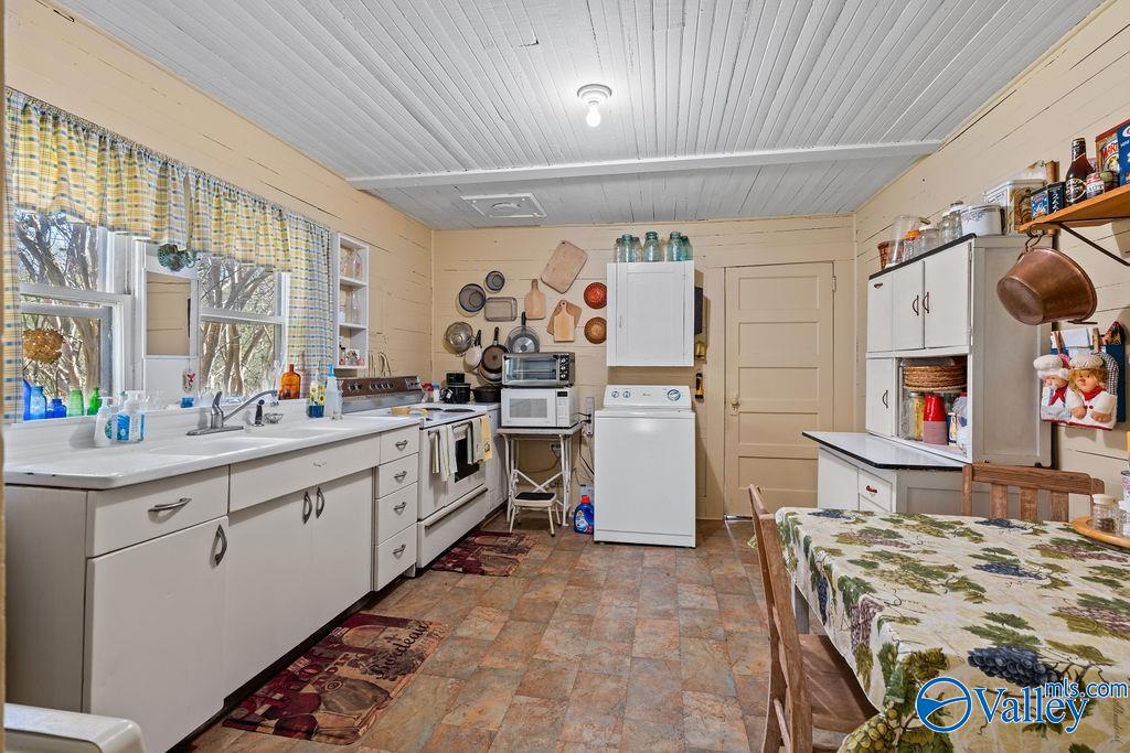 Kitchen with white cabinets, a double sink beneath curtained windows, and a dining table.