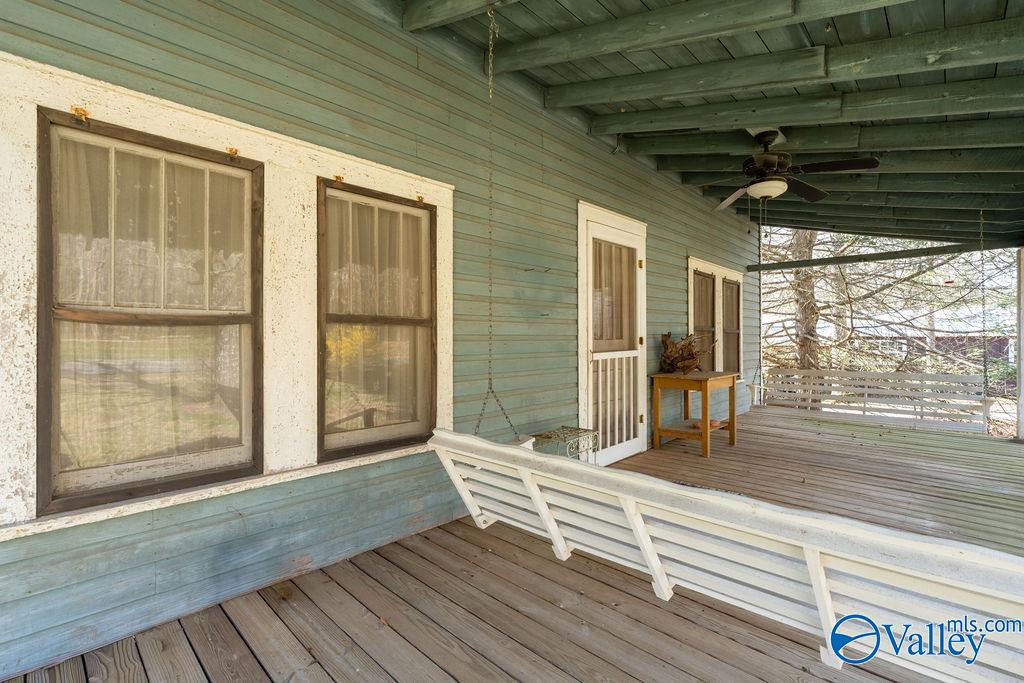 Covered porch with a white swing, weathered blue siding, and a ceiling fan.