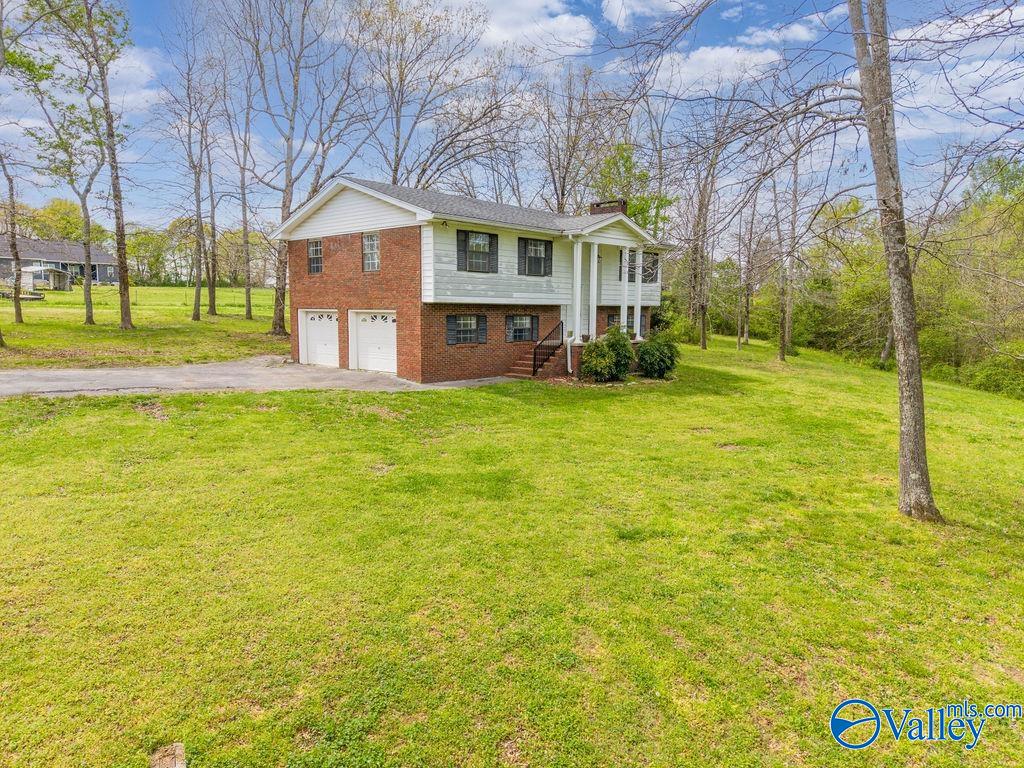 Split-level house with a brick lower level, white siding, two garage doors, and a broad lawn.