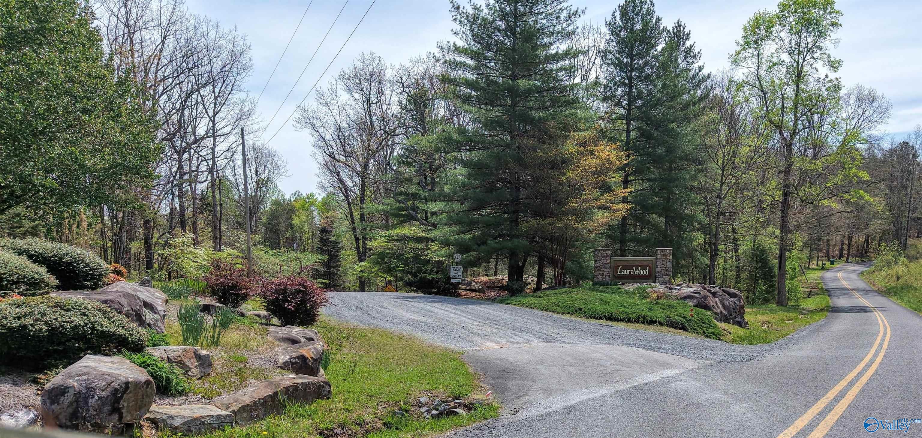 LauraWood community entrance with a stone sign, landscaped rocks, and a wooded roadside.