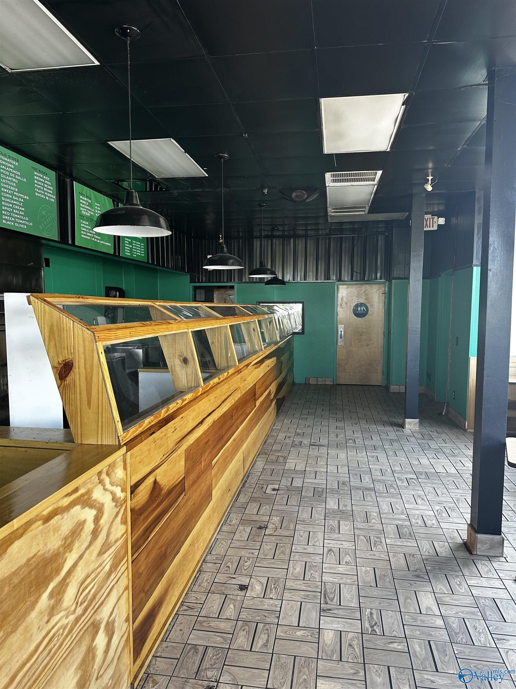 Commercial food-service interior with a long wooden display counter, teal walls, and patterned tile flooring.