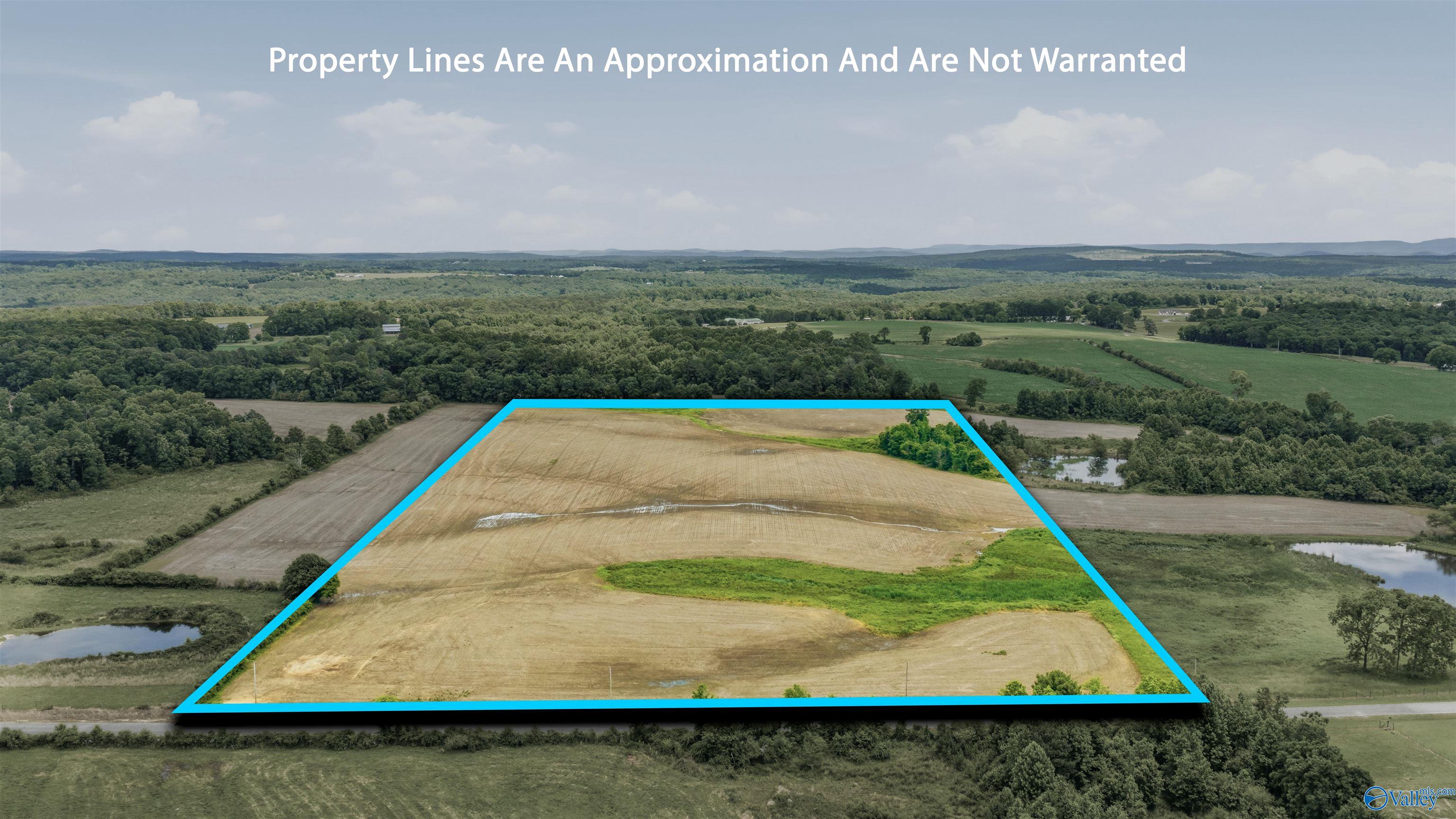 Aerial view of a harvested farmland parcel outlined in cyan, with wooded borders and ponds nearby.