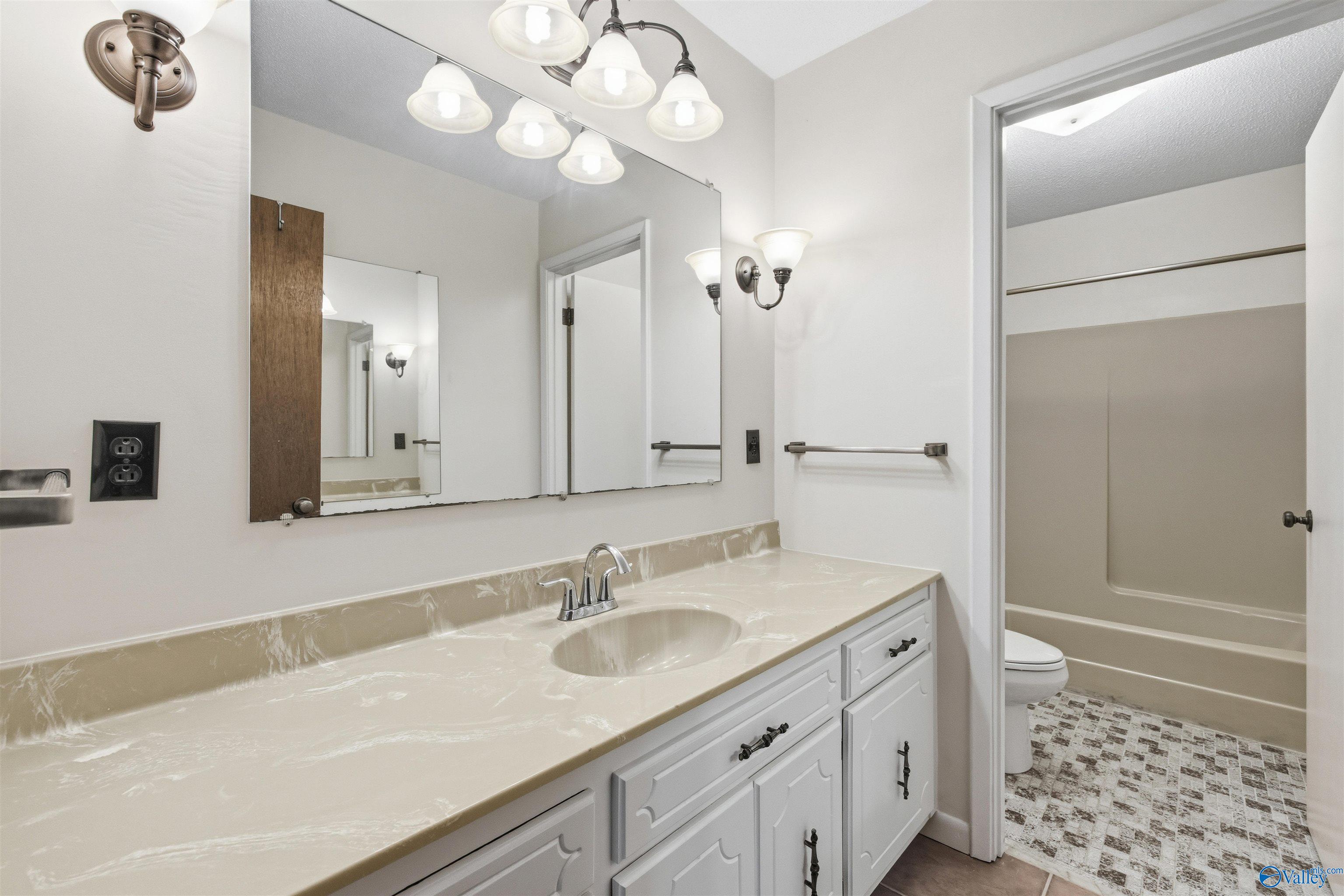 Bathroom with a long cream countertop, white vanity, large mirror, and adjoining tub and shower.