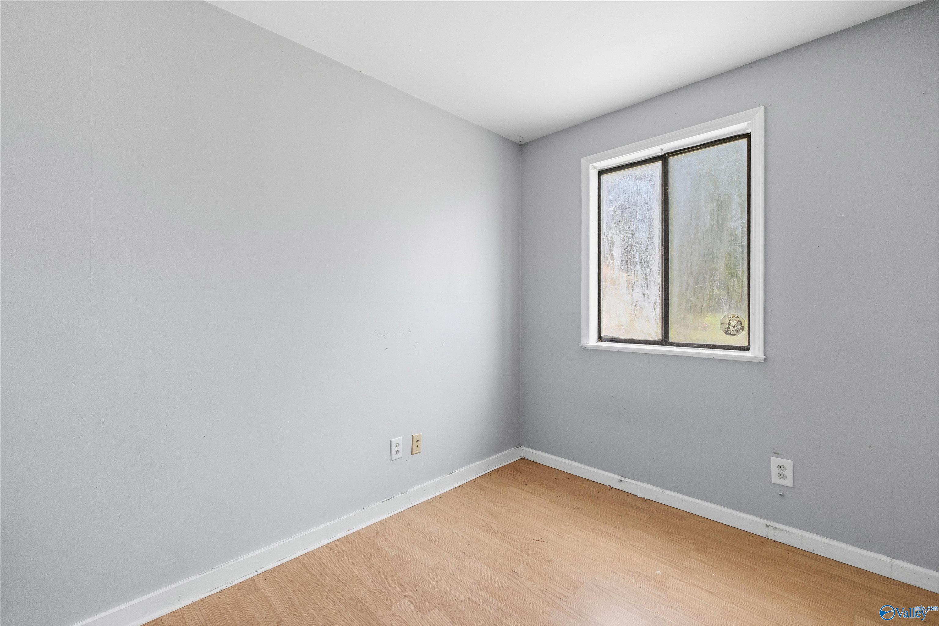 Empty room with gray walls, pale wood flooring, and a high two-pane window.