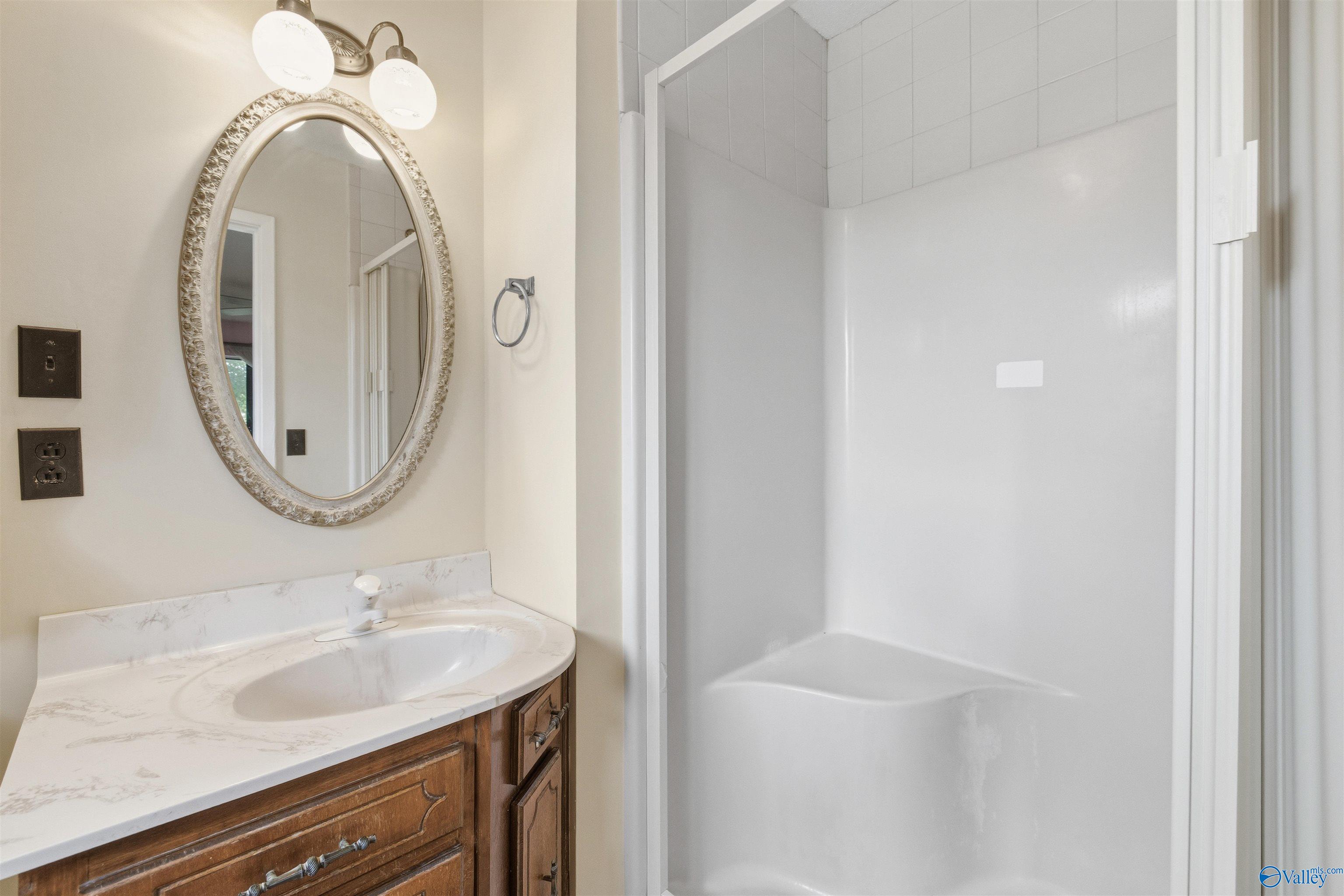 Bathroom with a dark wood vanity, ornate oval mirror, and white shower enclosure.