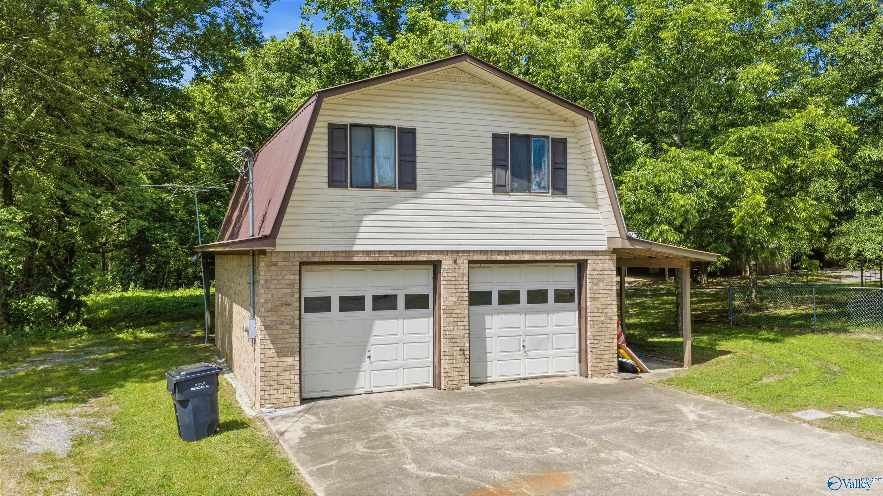 Cream-sided home with two garage doors, brick lower level, and attached carport among mature trees.