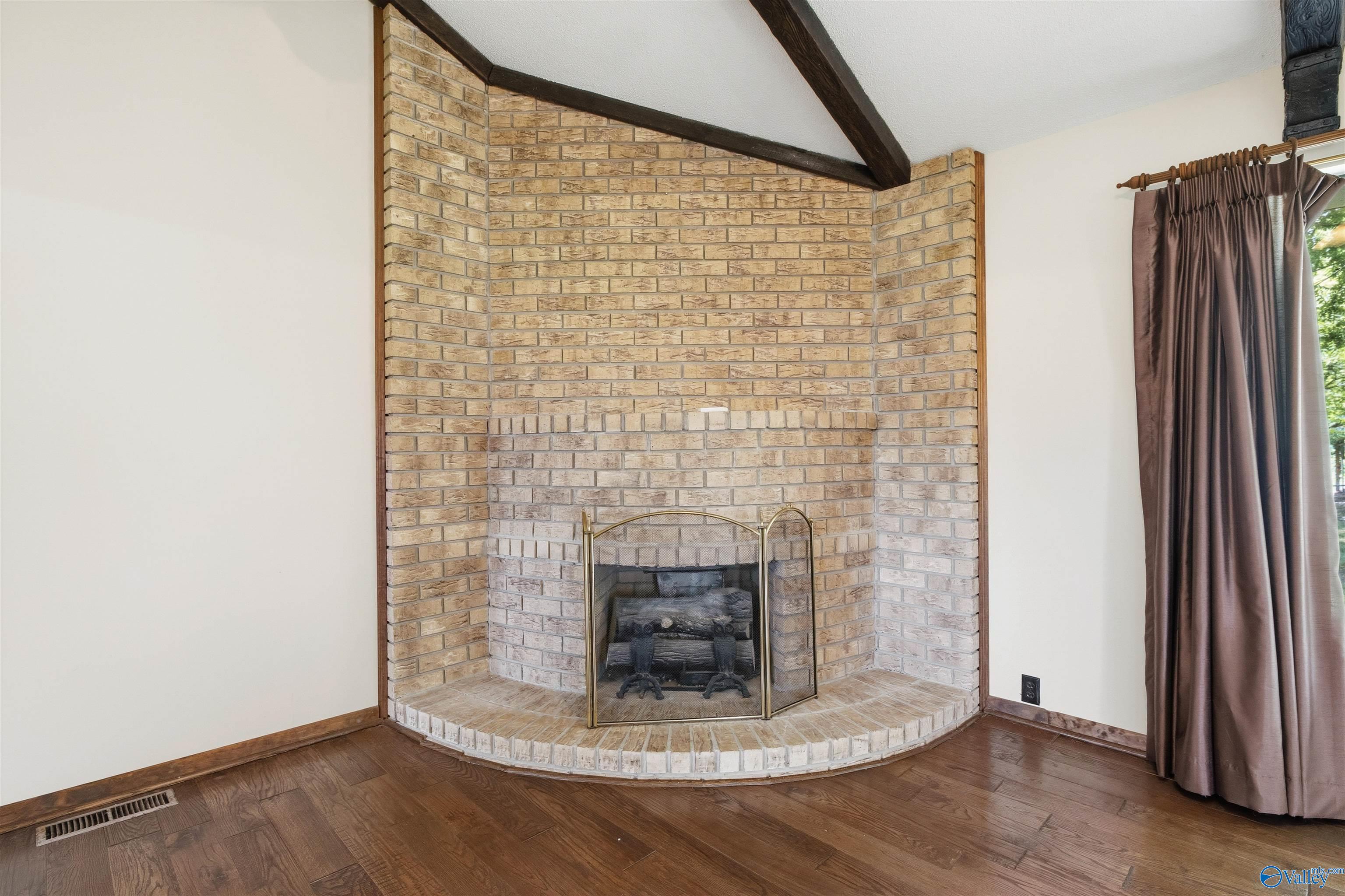 Living room with a tall brick fireplace, exposed ceiling beams, and dark hardwood floors.