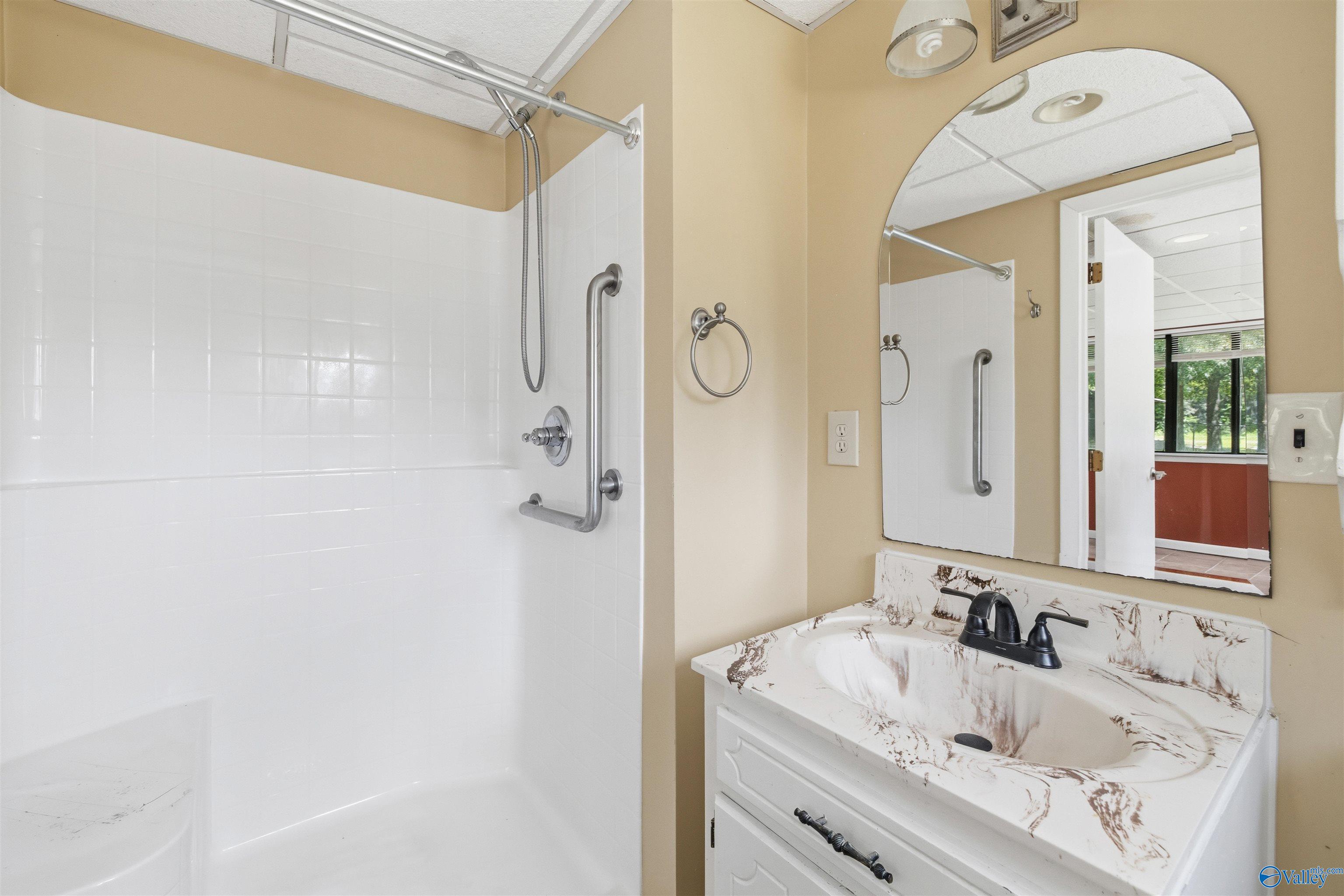 Bathroom with a tiled walk-in shower, chrome grab bars, and a white vanity with a veined sink.