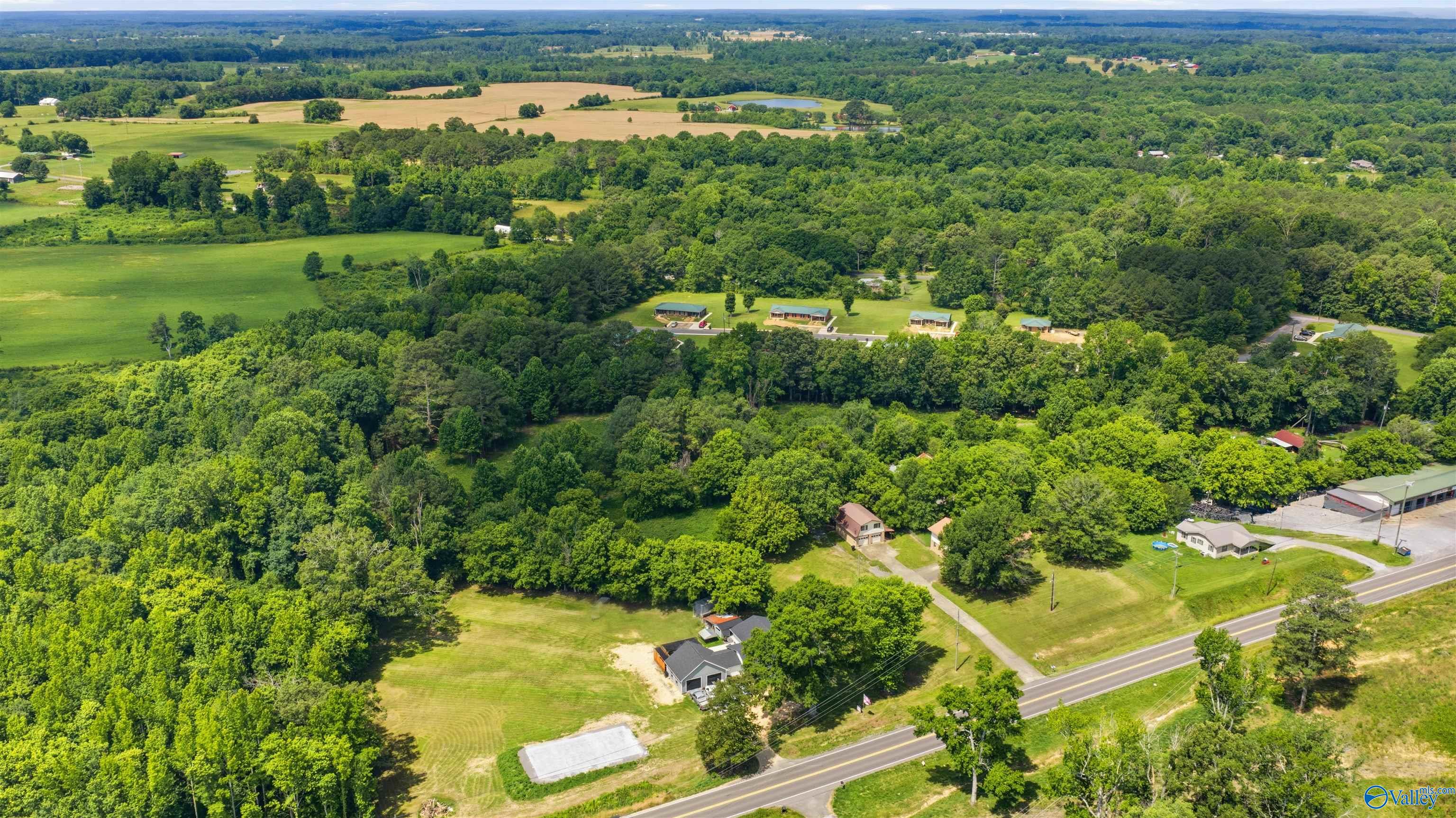 Aerial view of wooded acreage, scattered homes, open fields, and a road near Burton Drive.