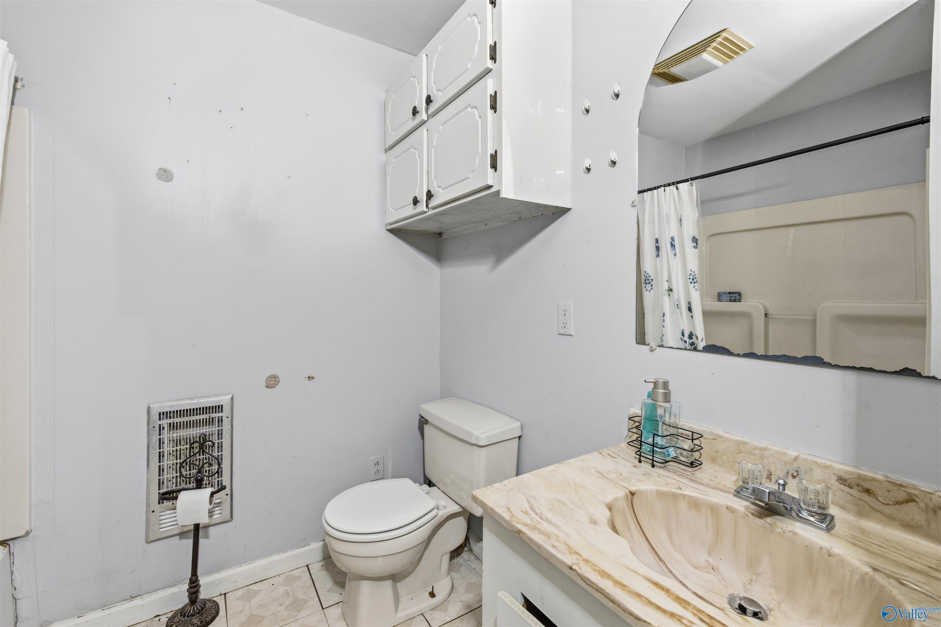 Bathroom with toilet, marble-look vanity, wall cabinet, and patterned shower curtain.