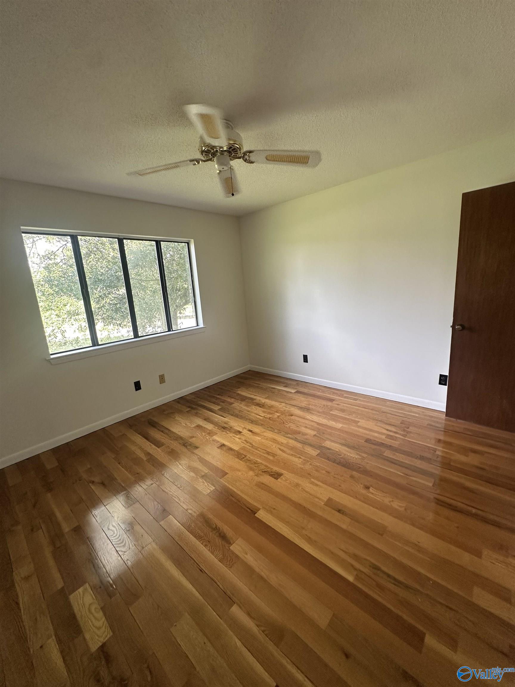 Empty room with polished wood floors, a large window, and a ceiling fan.
