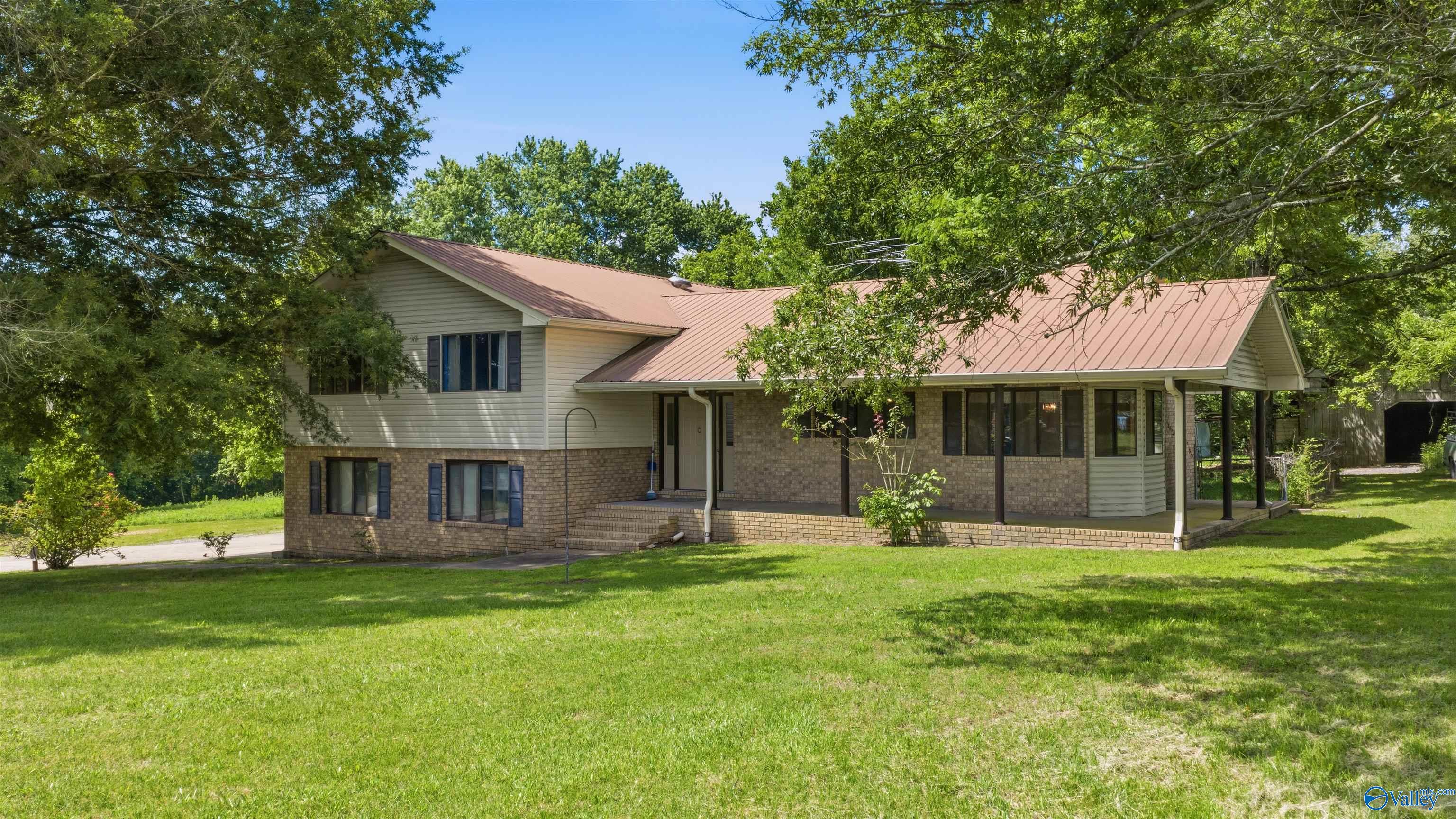 House exterior with brick lower walls, pale siding, a metal roof, and a broad lawn.