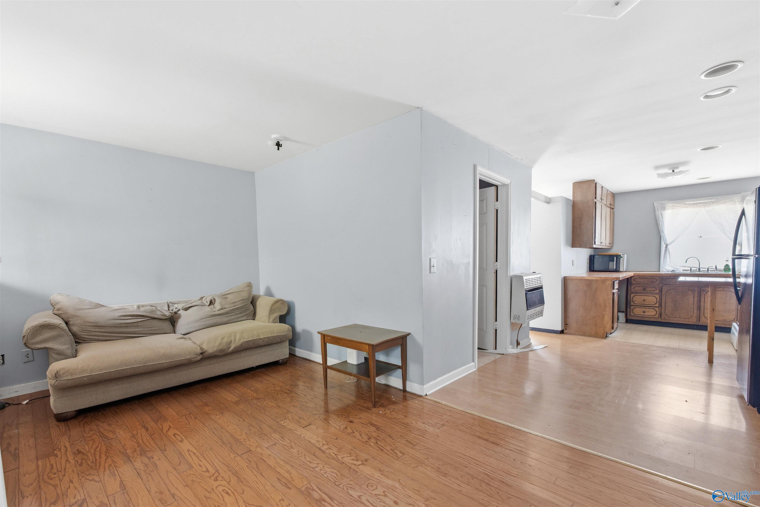 Living room with beige sofa and hardwood floors opening into a kitchen with wood cabinets.