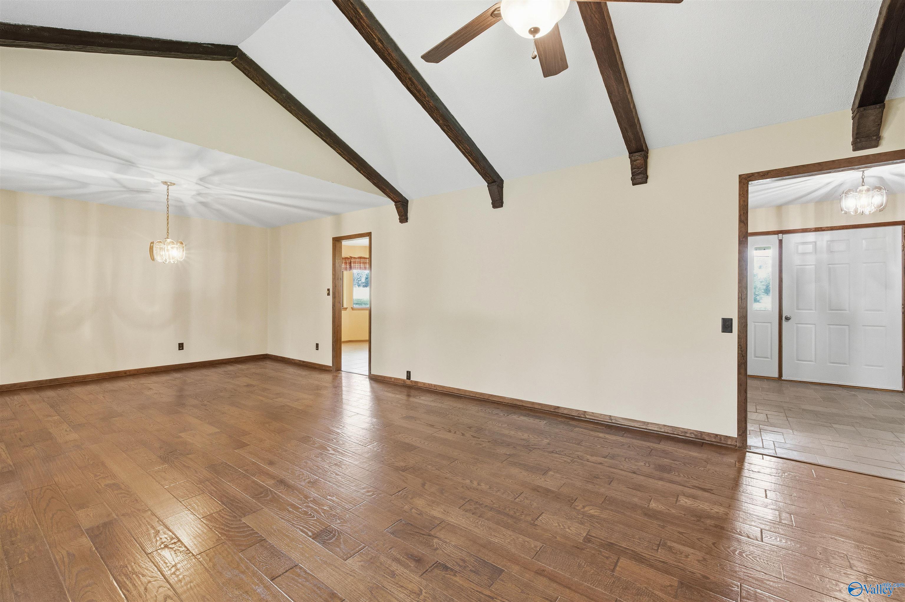Empty living room with glossy wood floors and exposed dark ceiling beams.