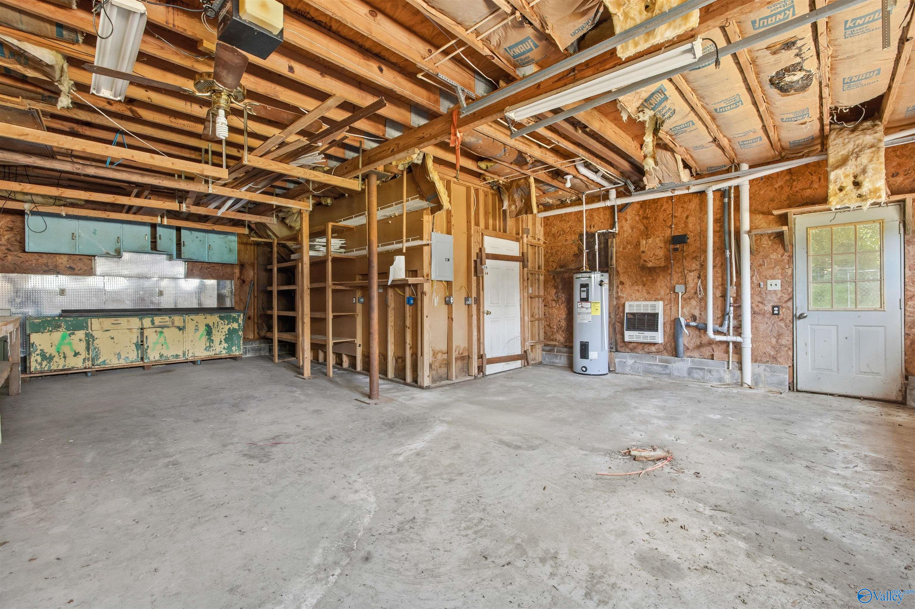 Unfinished garage with exposed ceiling framing, workshop cabinets, shelving, and a water heater.