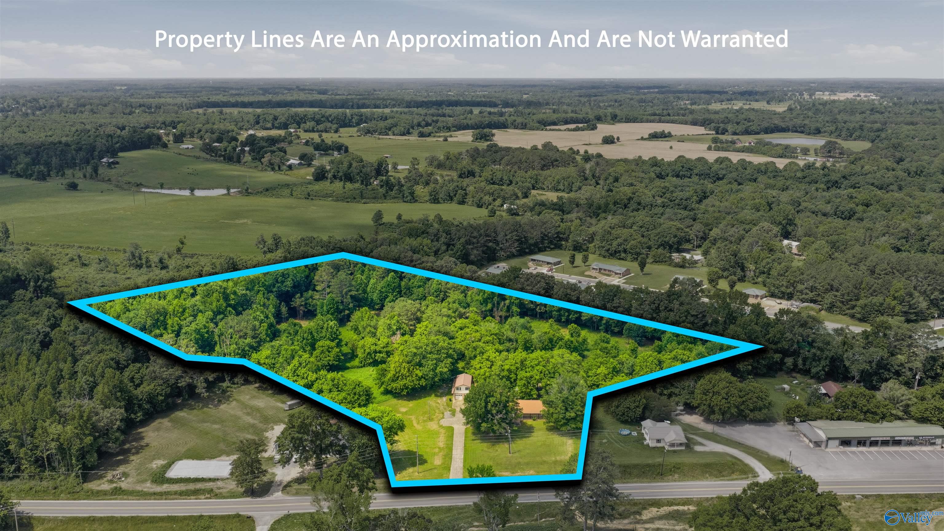 Aerial view of a wooded property outlined in blue, with a house and driveway near the road.