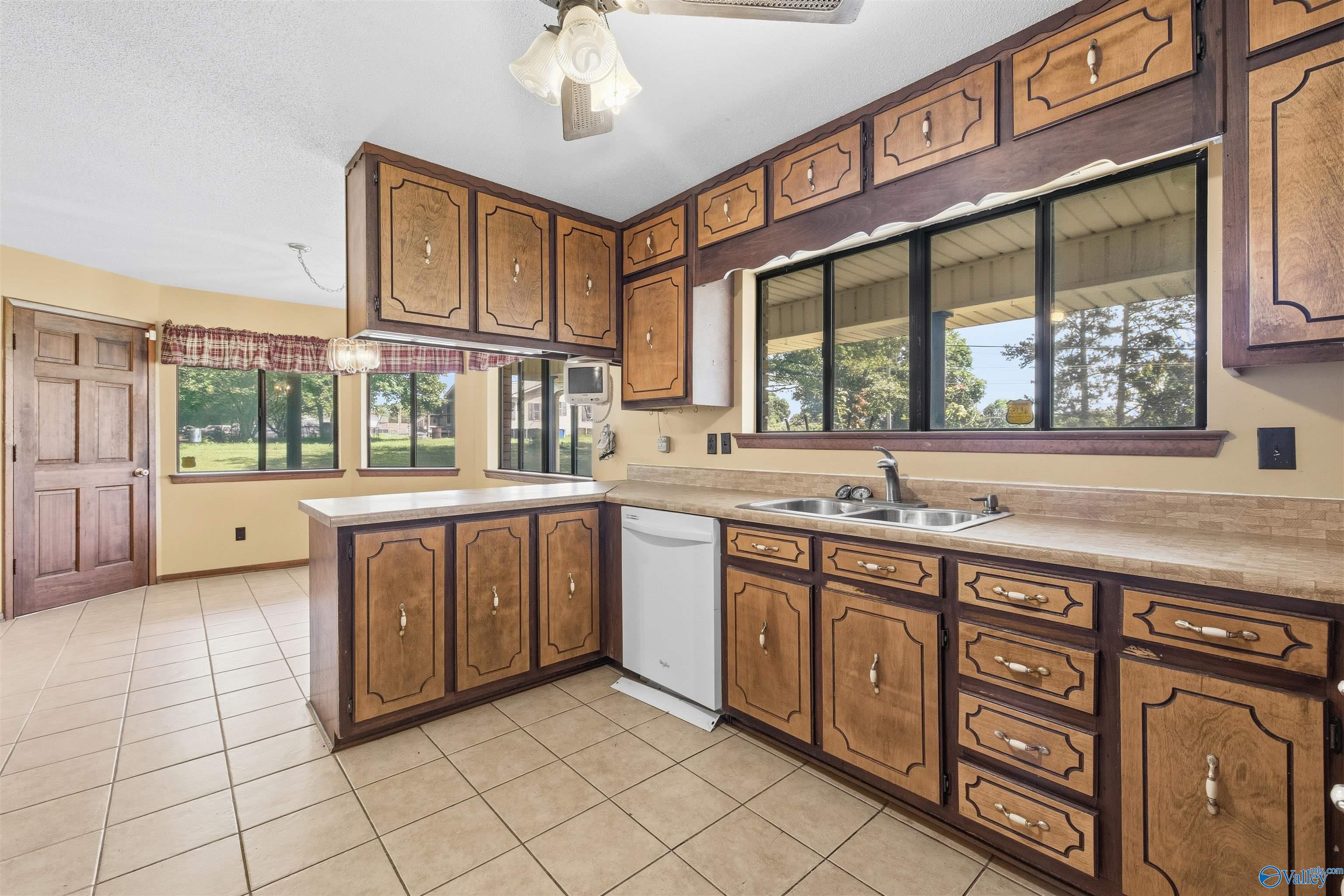 Kitchen with ornate brown cabinets, tiled floors, and wide windows above the sink.