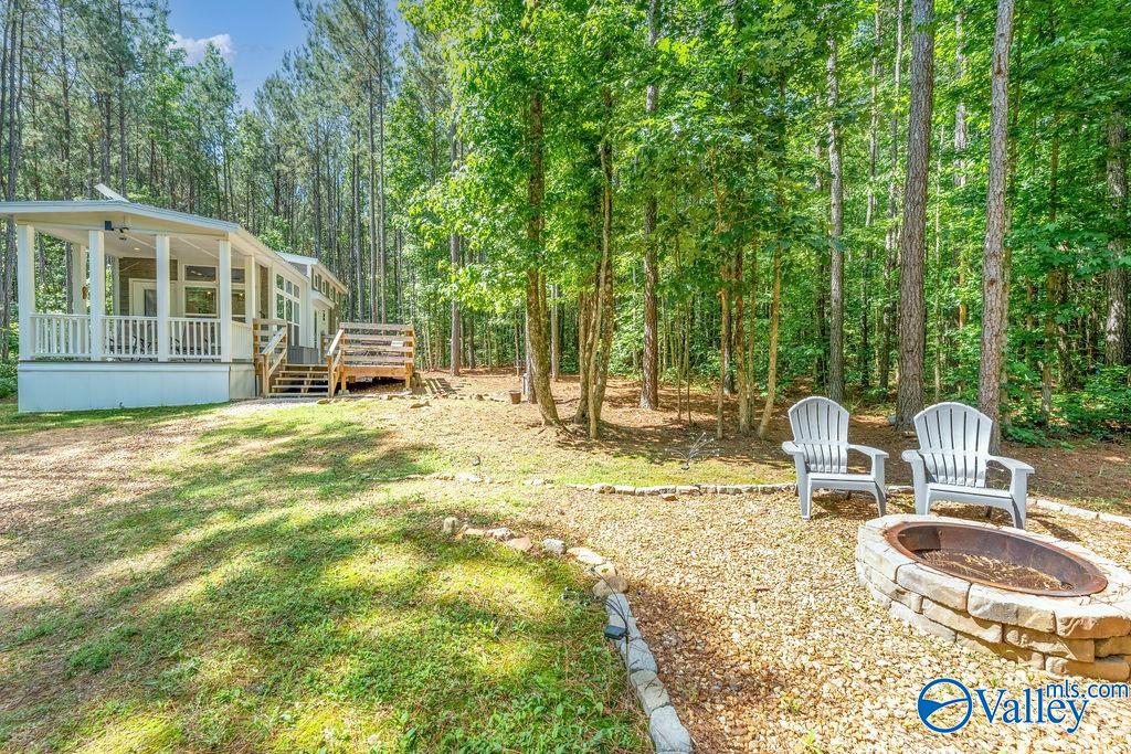 Wooded home with a covered porch, wooden deck, and stone fire pit seating area.