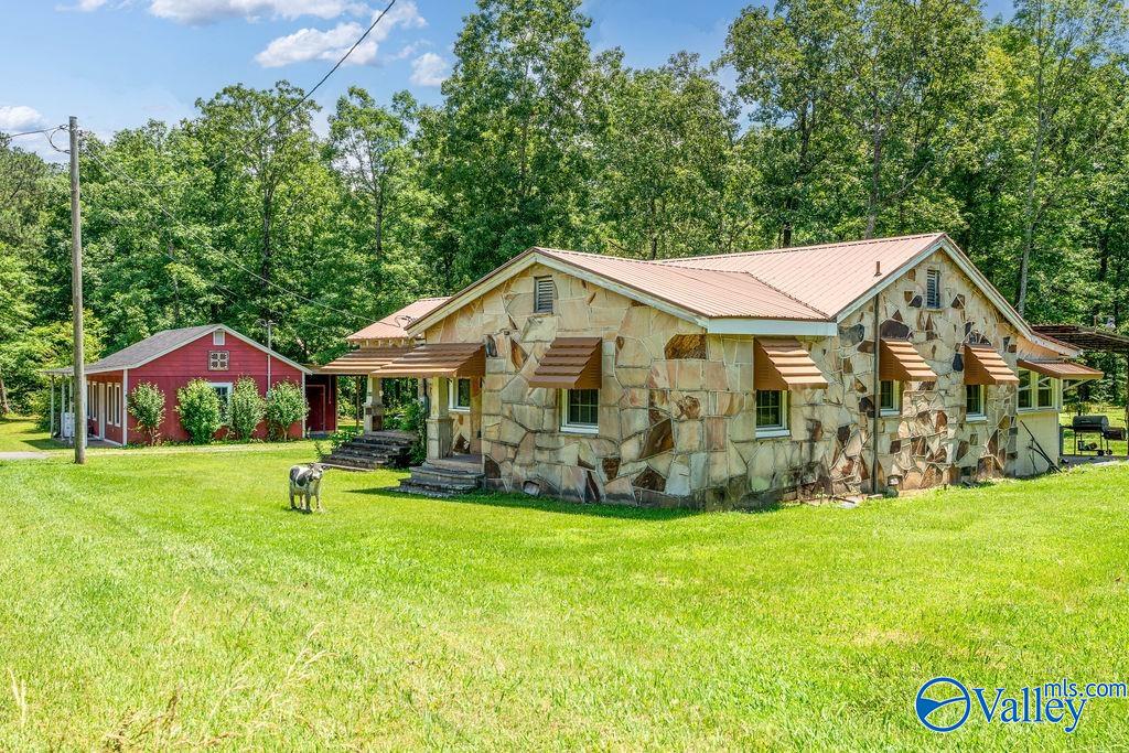 Stone-faced home with pale metal roof, red outbuilding, and dog on lawn.