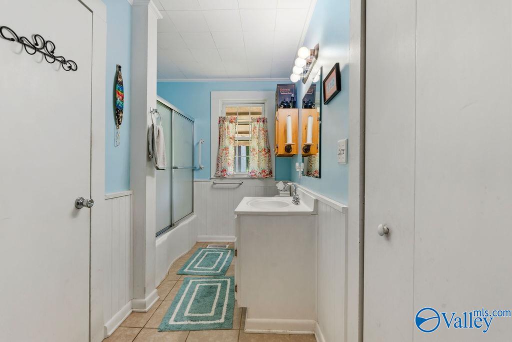 Bathroom with blue walls, glass shower enclosure, white vanity, floral curtains, and teal rugs.