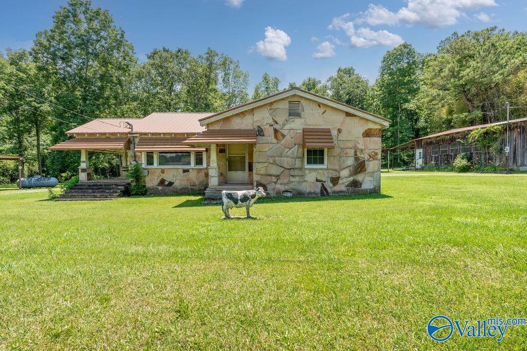Stone house with covered carport and a cow standing on the front lawn.