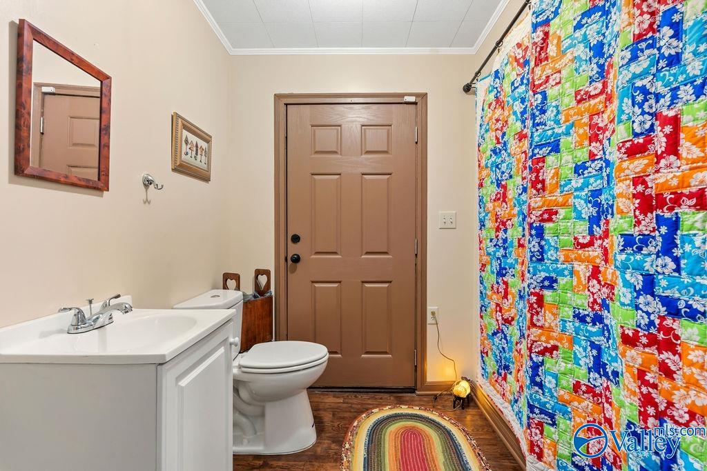 Bathroom with a white vanity, toilet, colorful patchwork shower curtain, and striped rug.