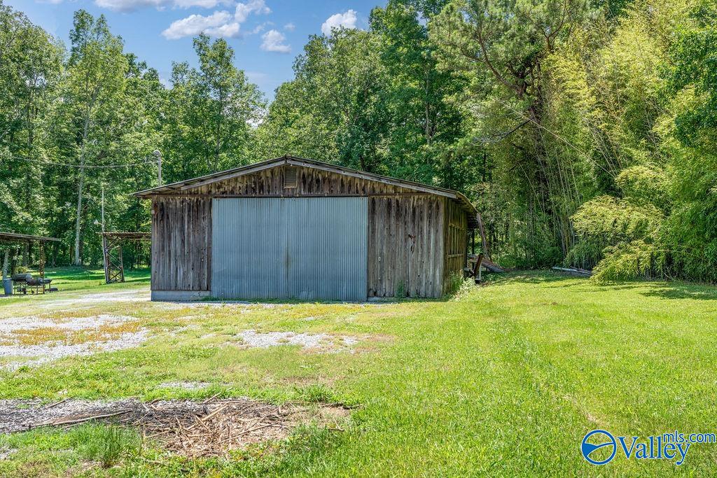 Weathered wooden outbuilding with a large metal roll-up door in a wooded grassy clearing.