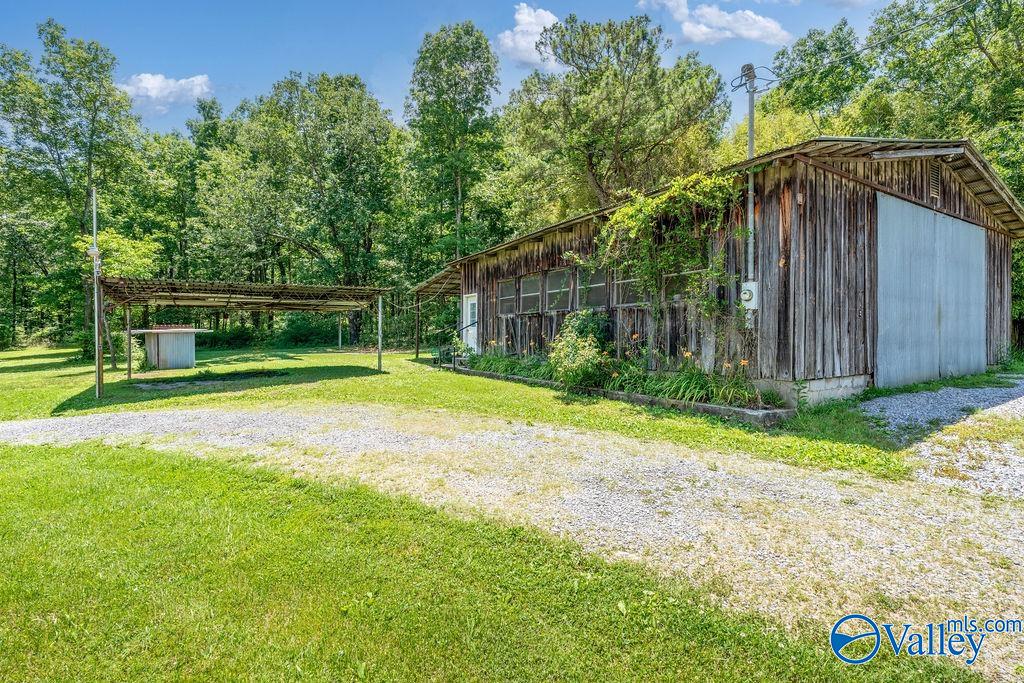 Wooden workshop with a metal sliding door and open-sided carport beside a gravel drive.