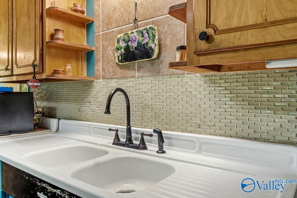 Kitchen sink beneath a pale green tile backsplash, framed by honey-colored wood cabinets.
