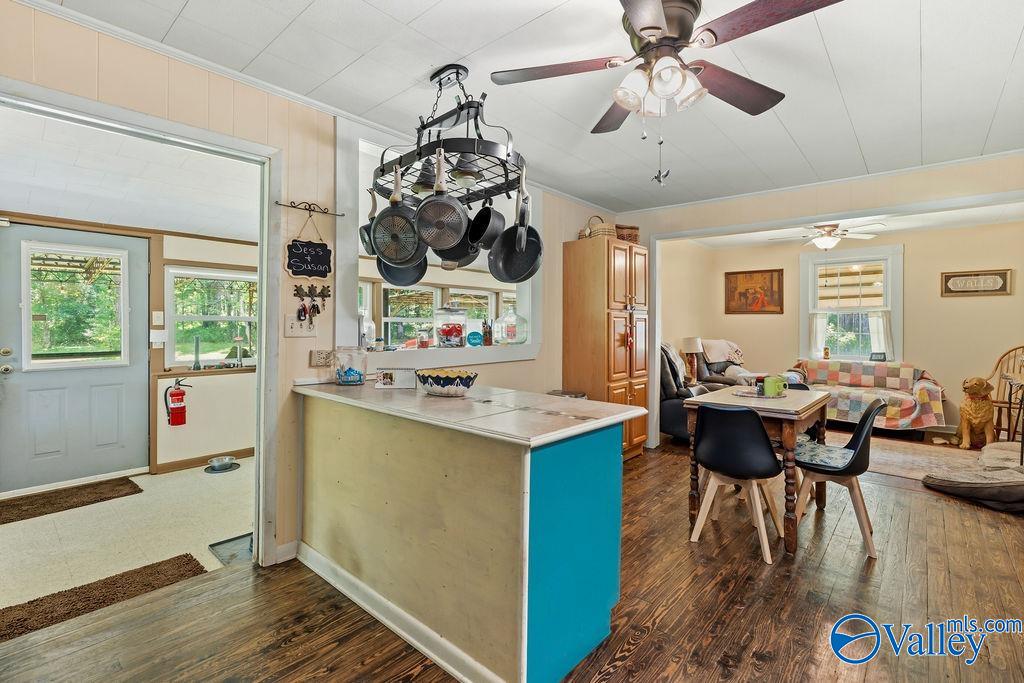 Kitchen and dining area opening into a living room, with a blue-sided peninsula and hanging pot rack.