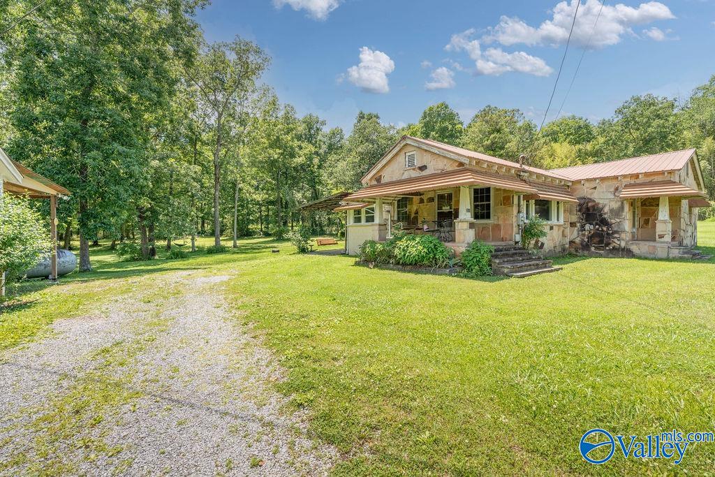 Rural home with a covered porch, metal roofs, gravel driveway, and broad lawn.