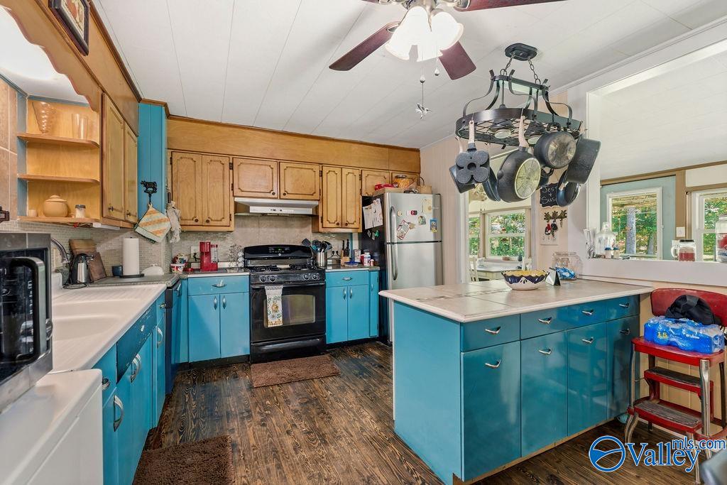 Kitchen with turquoise cabinets, a large island, wood upper cabinets, and hanging pots and pans.