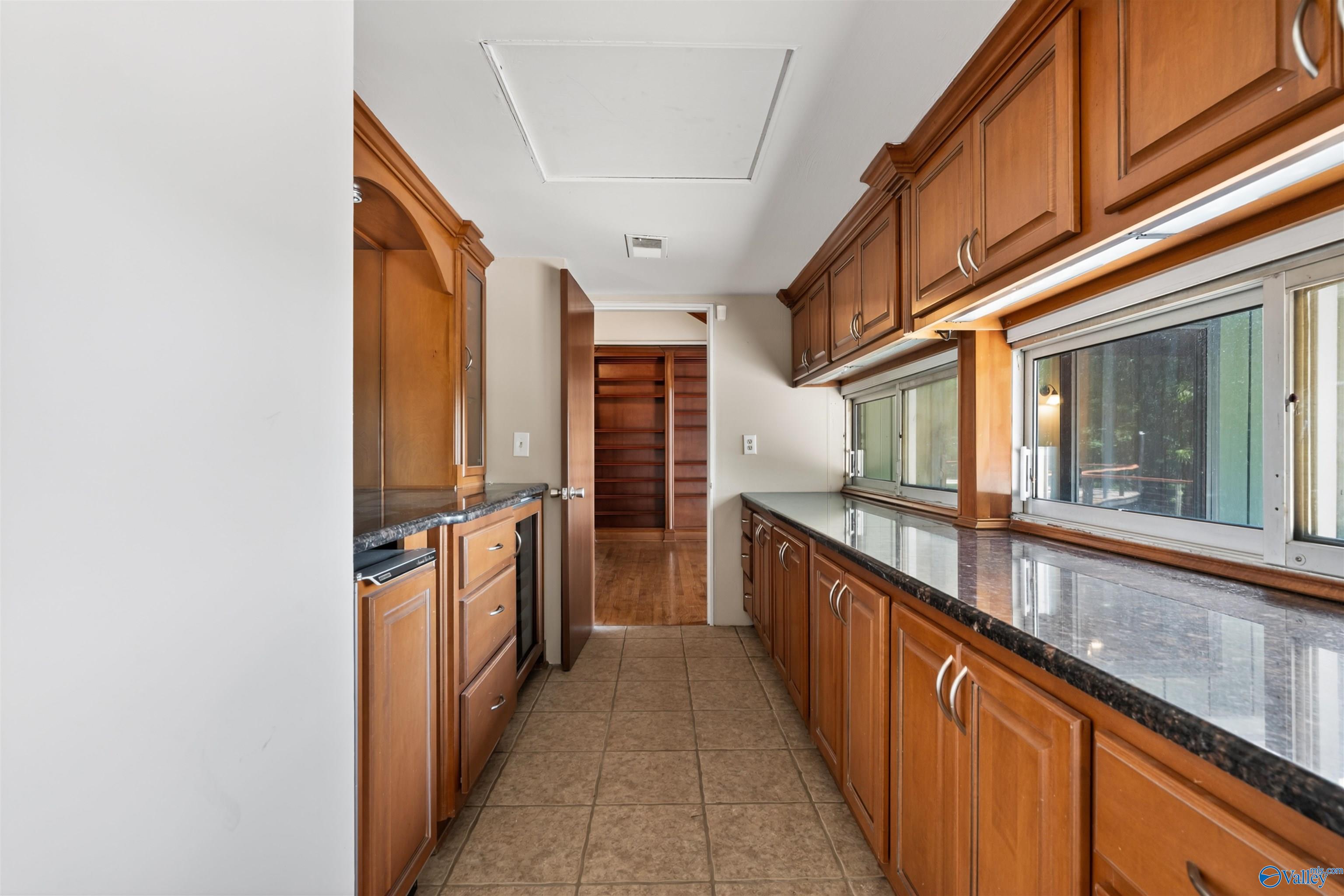 Galley kitchen with warm wood cabinets, dark stone countertops, and long windows above the counter.