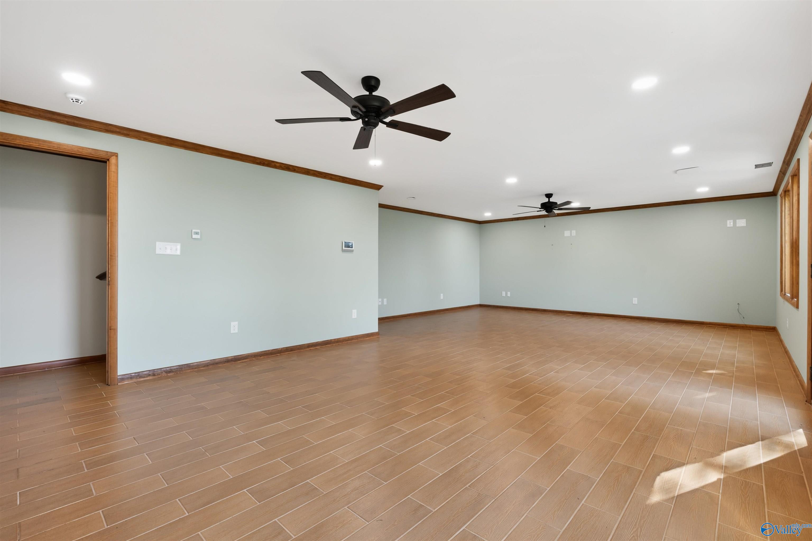 Spacious vacant room with wood-look tile flooring, two ceiling fans, and wood trim.