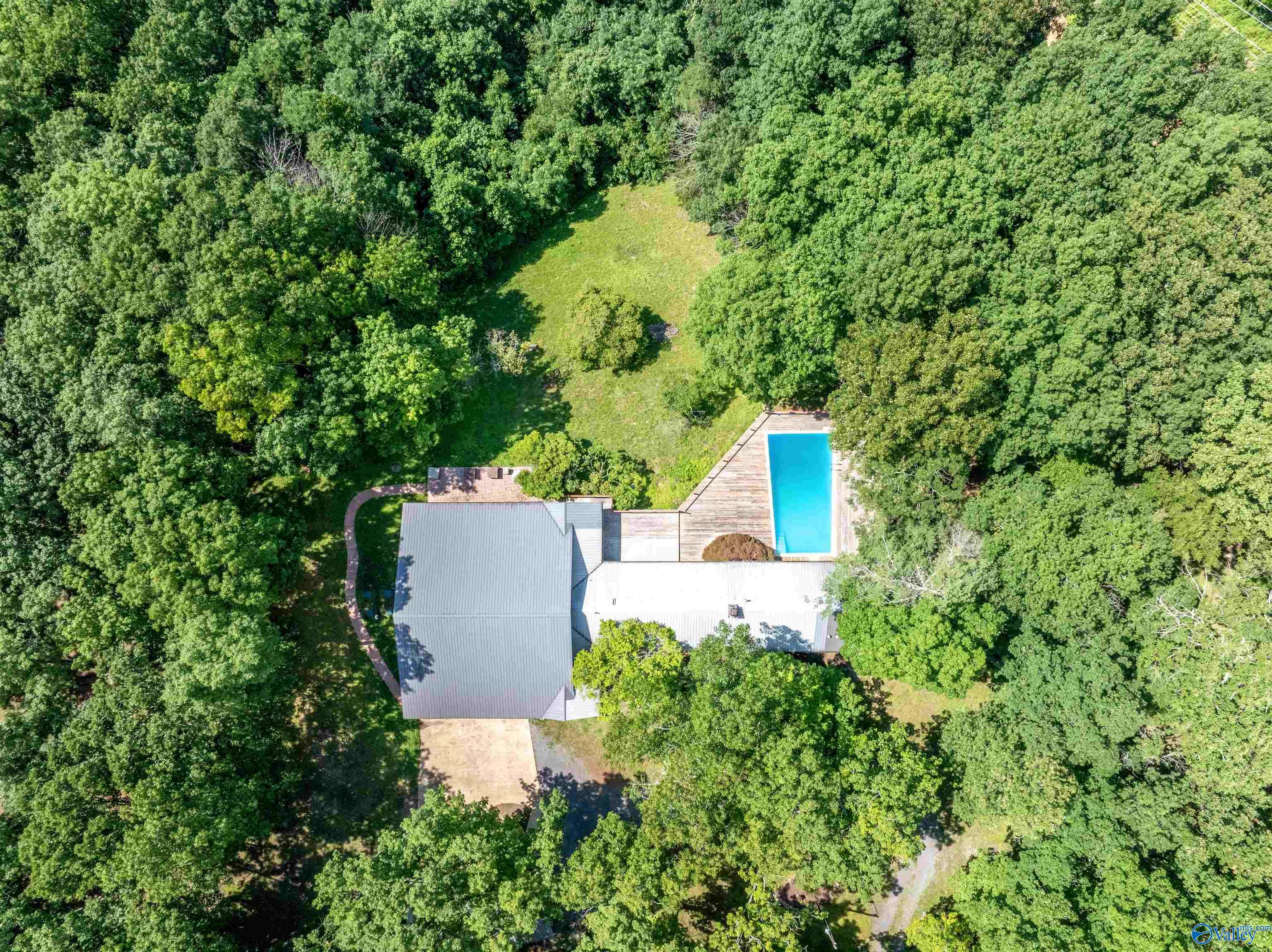 Aerial view of a wooded property with a house, swimming pool, and grassy clearing.