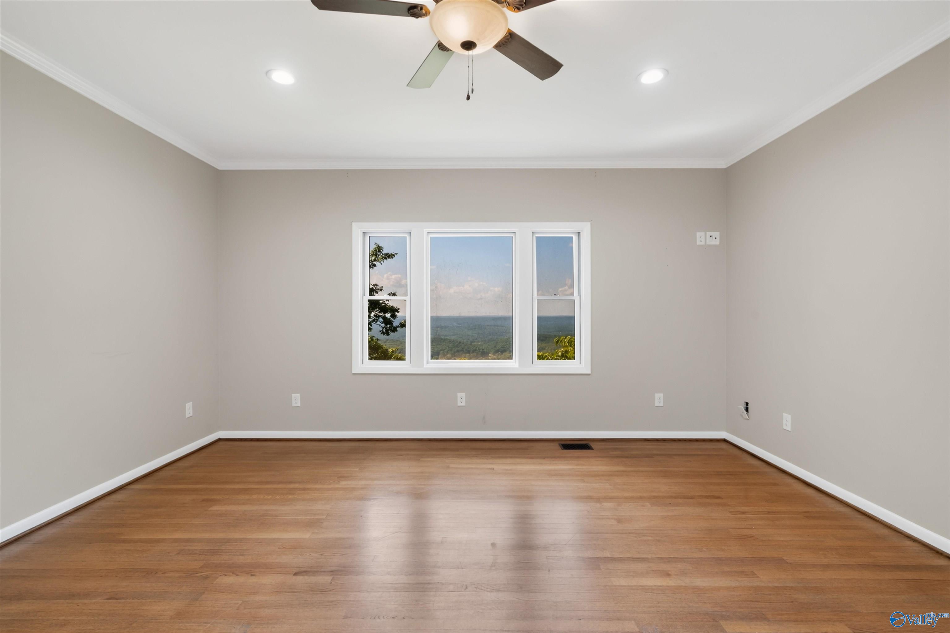 Empty room with hardwood floors and a wide window overlooking a green valley.