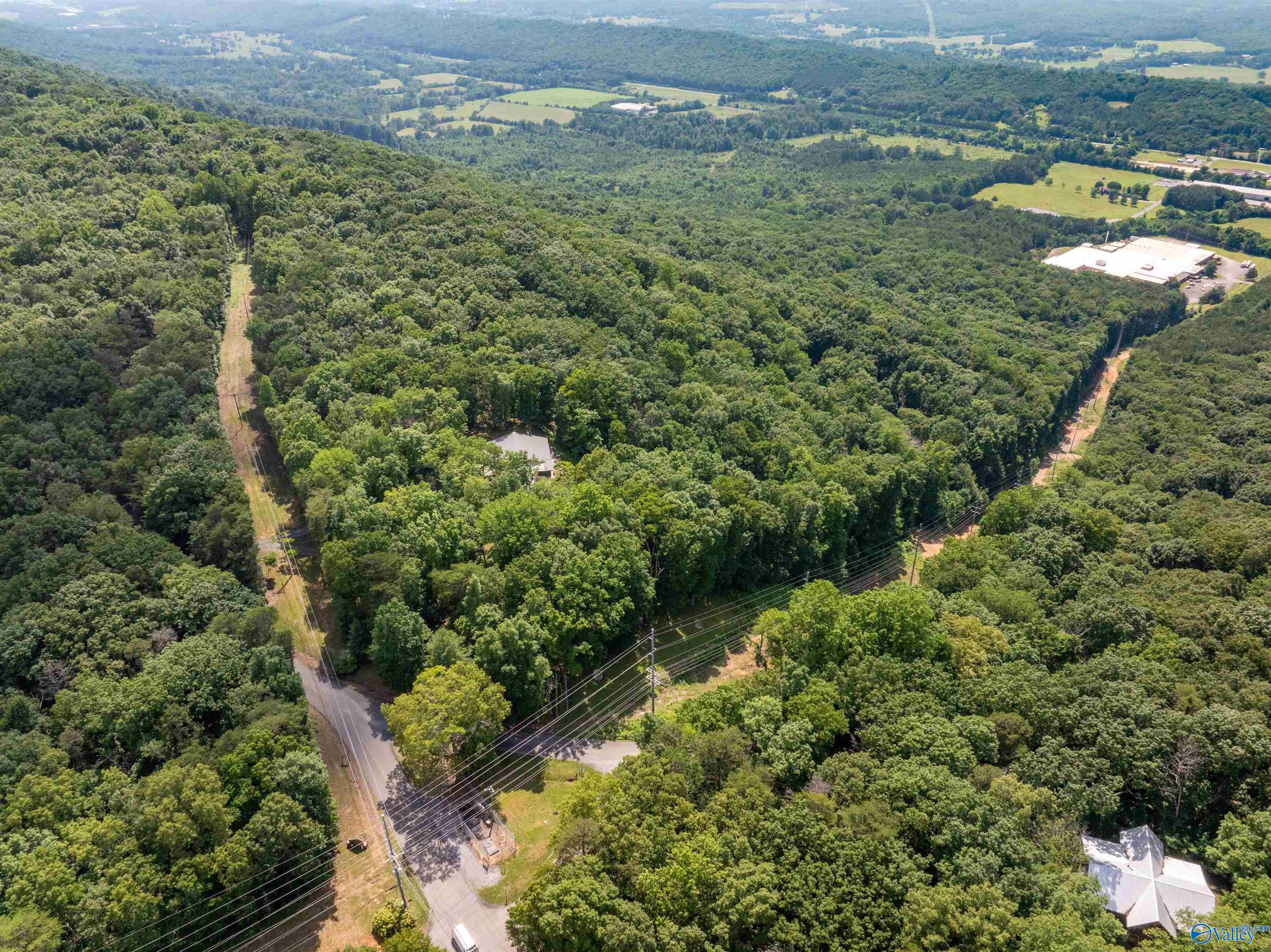 Aerial view of a wooded property with a small house, road access, and surrounding countryside.