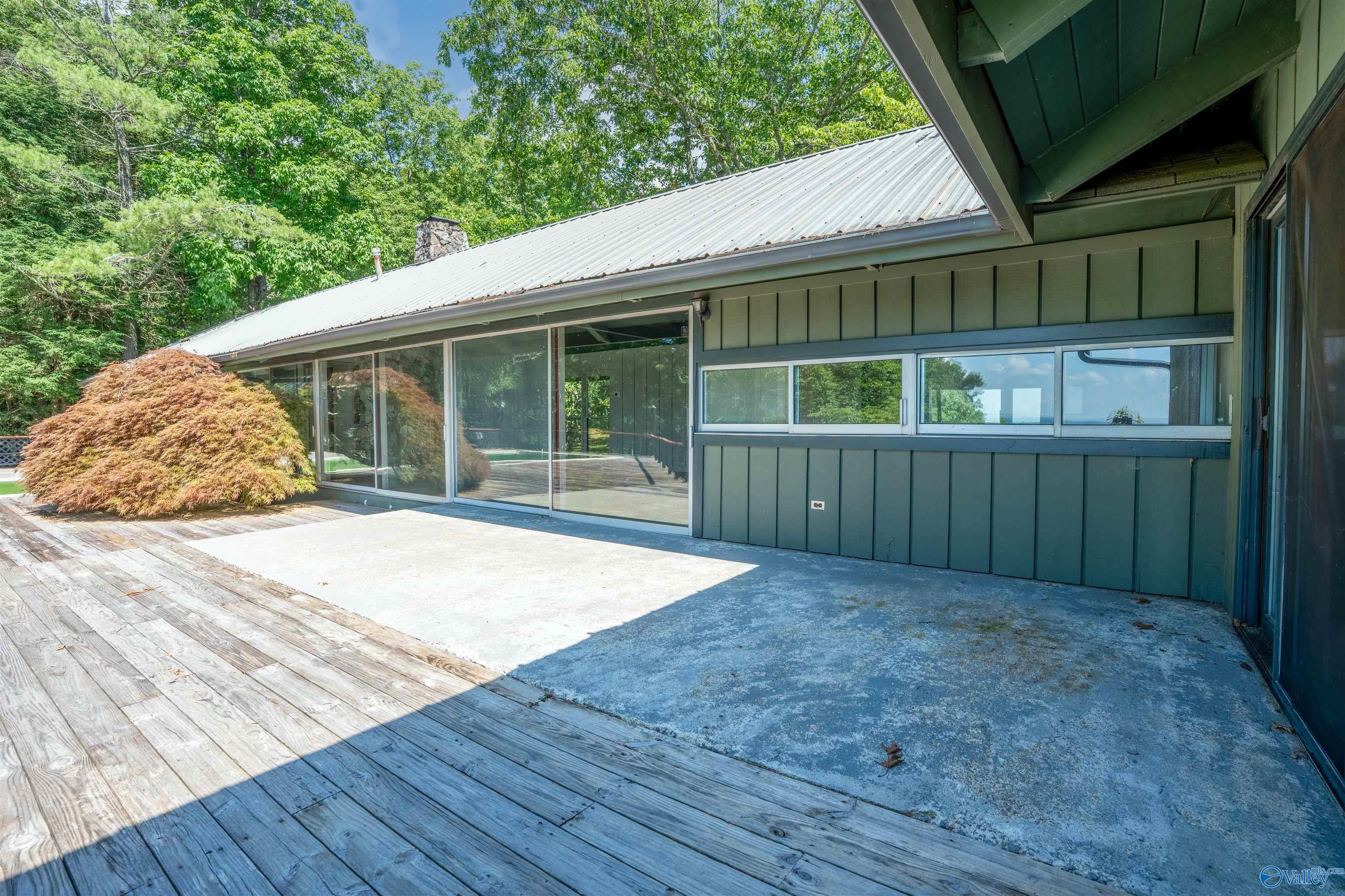 Home’s rear patio with broad wood decking, concrete paving, sliding glass doors, and mature landscaping.