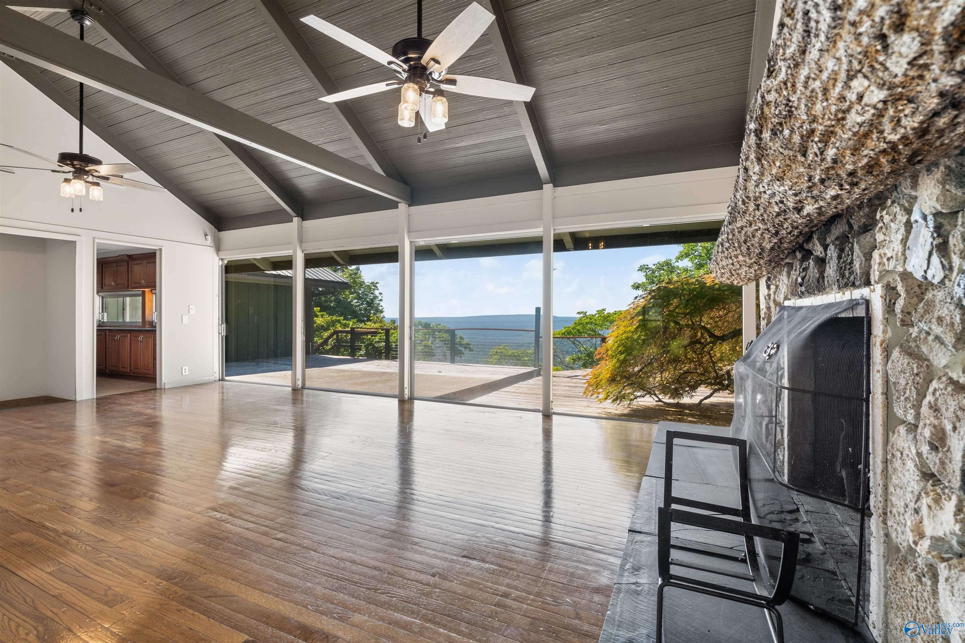 Living room with vaulted beam ceiling, stone fireplace, and sliding doors opening onto a mountain-view deck.