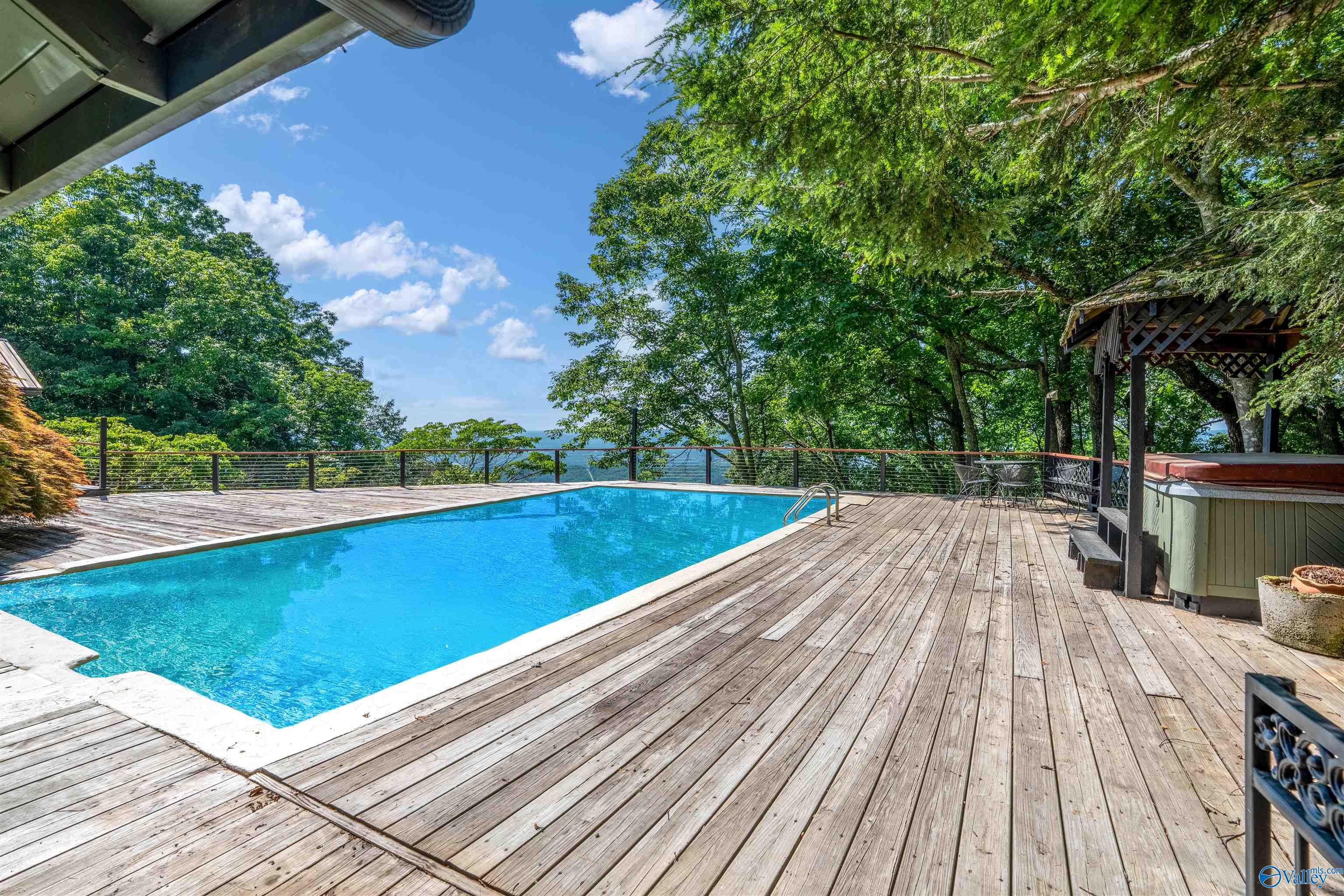 Swimming pool on a spacious wooden deck, with a covered hot tub and distant water view.