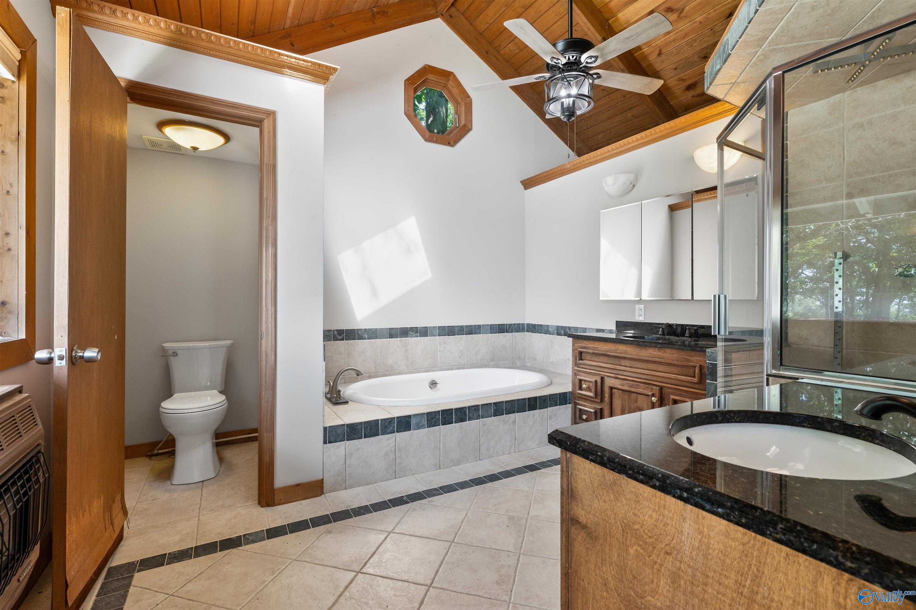Bathroom with a built-in soaking tub, glass shower, wood vanities, and a vaulted wood ceiling.