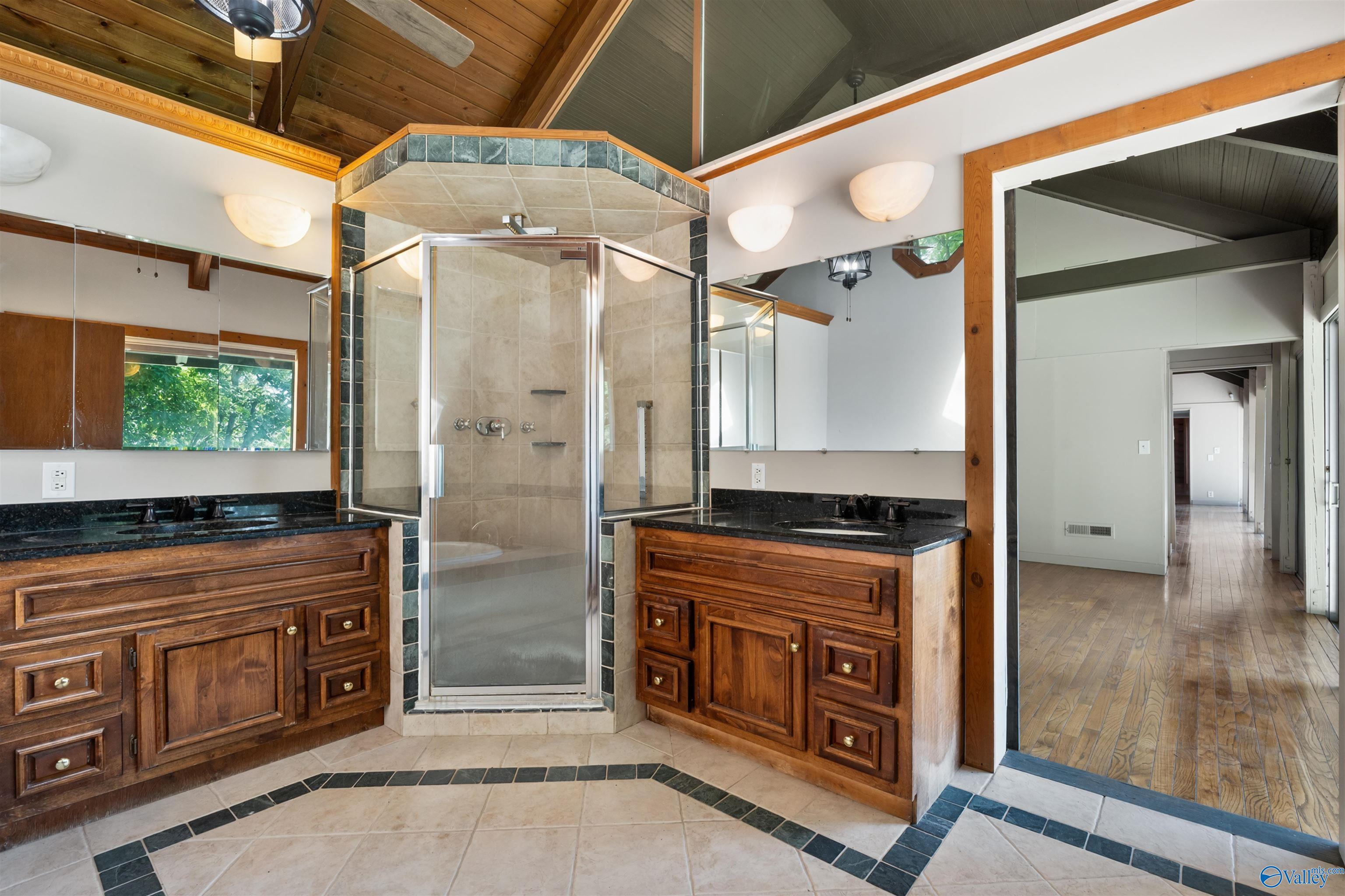 Bathroom with a tiled glass shower, double wooden vanities, and a vaulted wood ceiling.